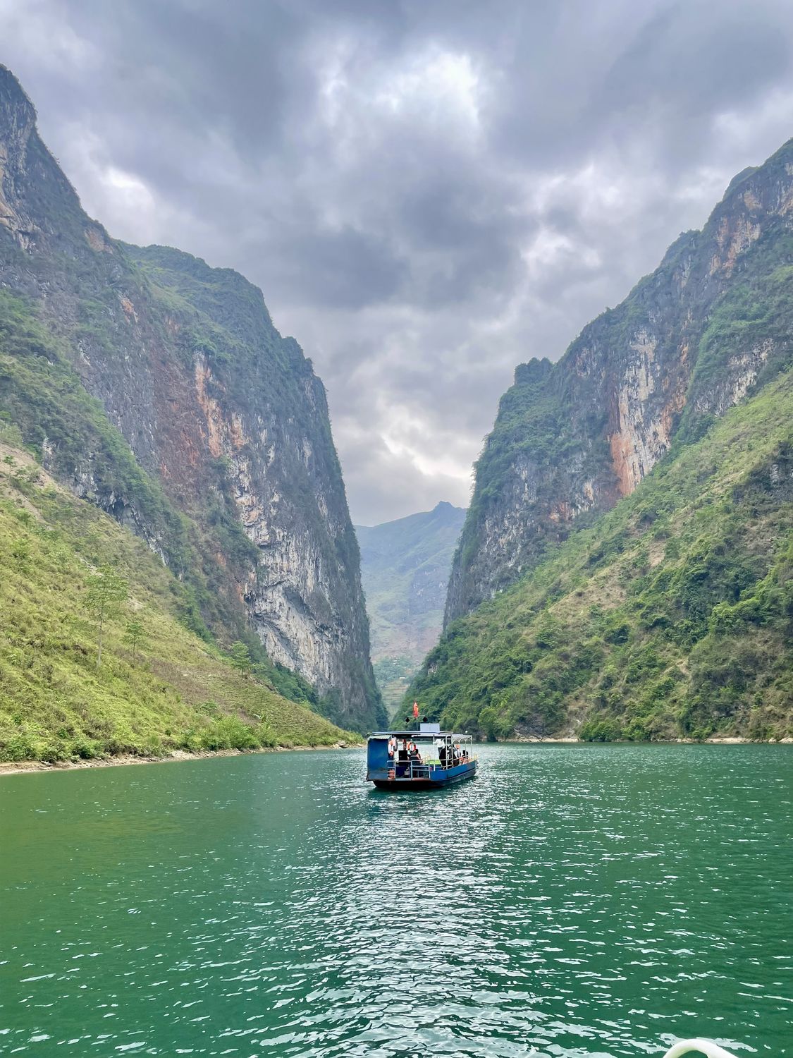 A small ferry on green water between limestone cliffs